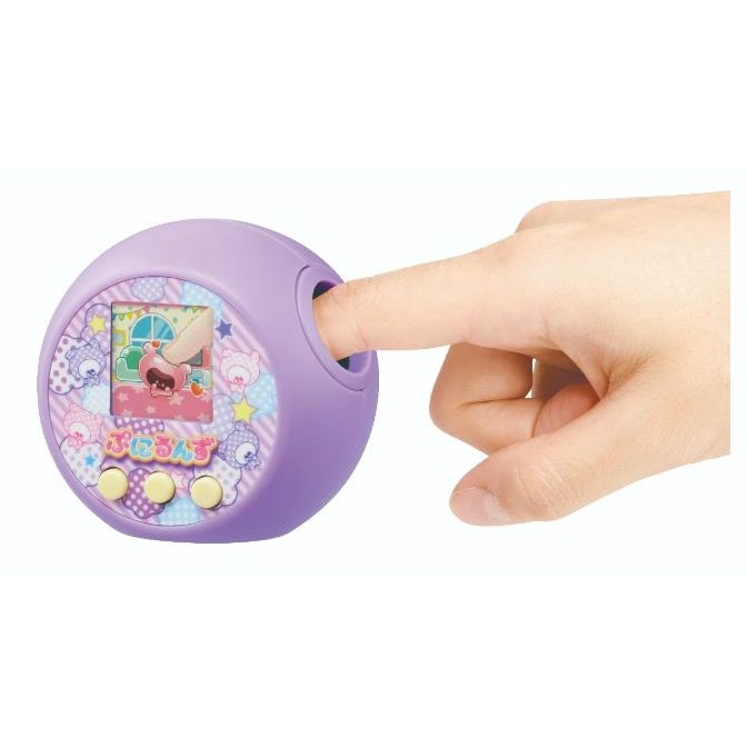  Purple Tamagotchi-like toy with a finger pressing the top. Screen shows a cartoon character.