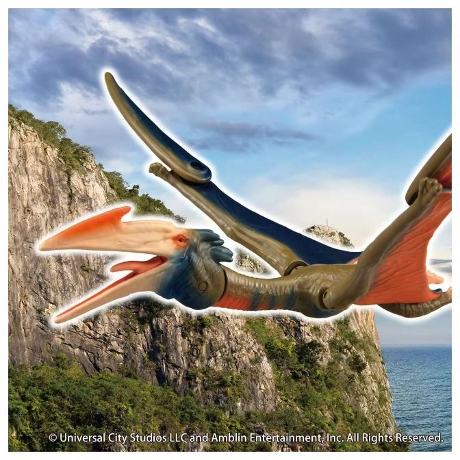  Pterodactyl toy with articulated wings, orange beak, and blue body against a cliff and sky backdrop.