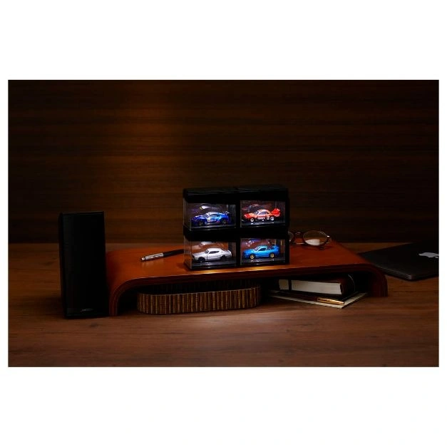  Four toy cars displayed in a black case on a wooden desk with a laptop and glasses.