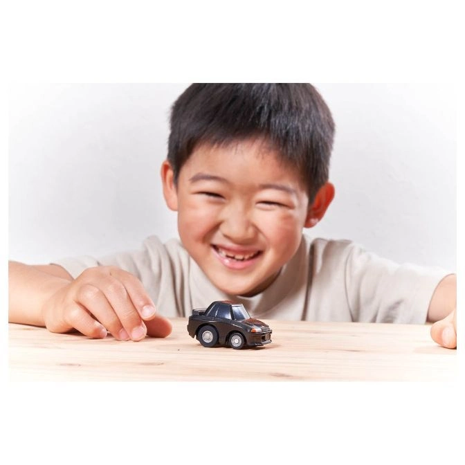  Smiling child playing with a small, black toy car on a wooden table.