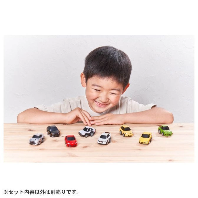 Smiling boy looking at toy cars on a wooden table. Assorted colors and models.