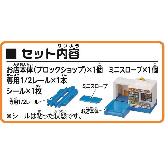  The image shows a set of toy train tracks and a building. The set includes a store building, a mini slope, a 1/2 rail, and a sticker sheet. The store building is white with a blue base and a yellow roof. The mini slope is blue and has a slight incline. The 1/2 rail is blue and has two tracks. The sticker sheet is not visible in the image.