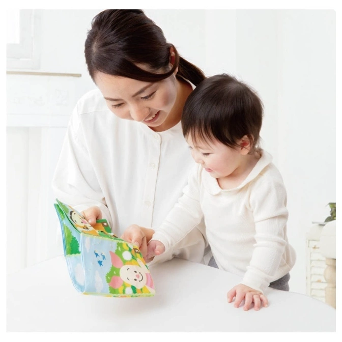  Baby and woman looking at soft book with animal illustrations on a white table.