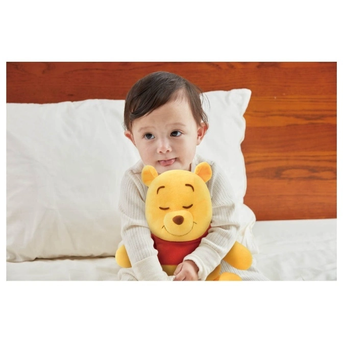  Baby hugging a plush Winnie the Pooh toy with closed eyes, wearing a red shirt.