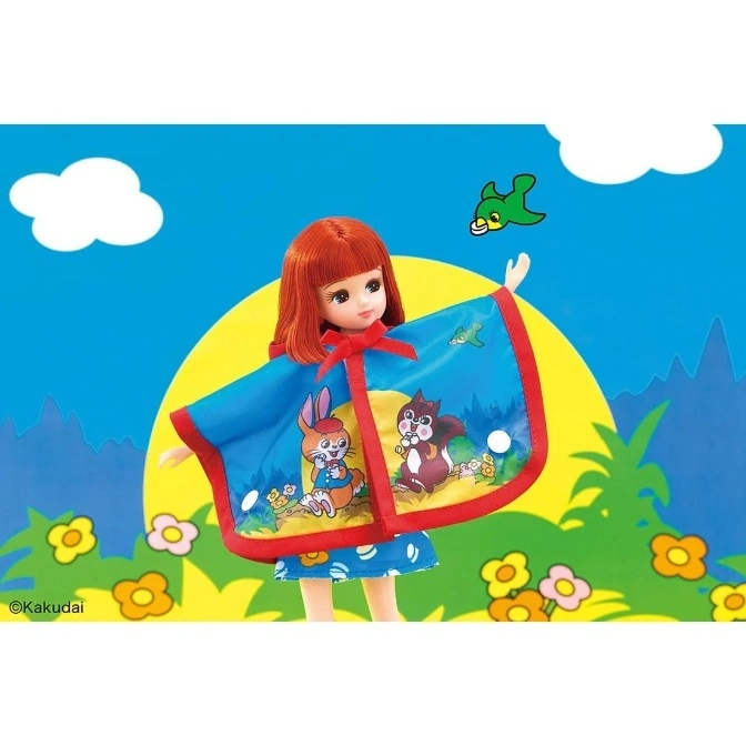  Red-haired doll wearing a blue cape with cartoon animals, standing against a bright, illustrated background.
