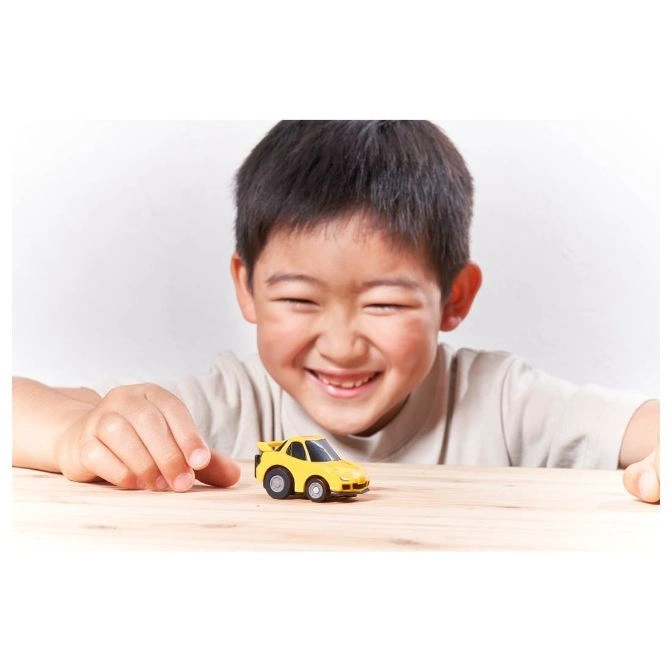  Smiling child playing with a yellow toy car on a wooden table.