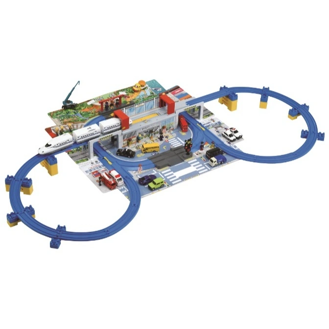 Toy train set with a bullet train, station, cars, and a circular blue track on a playmat.