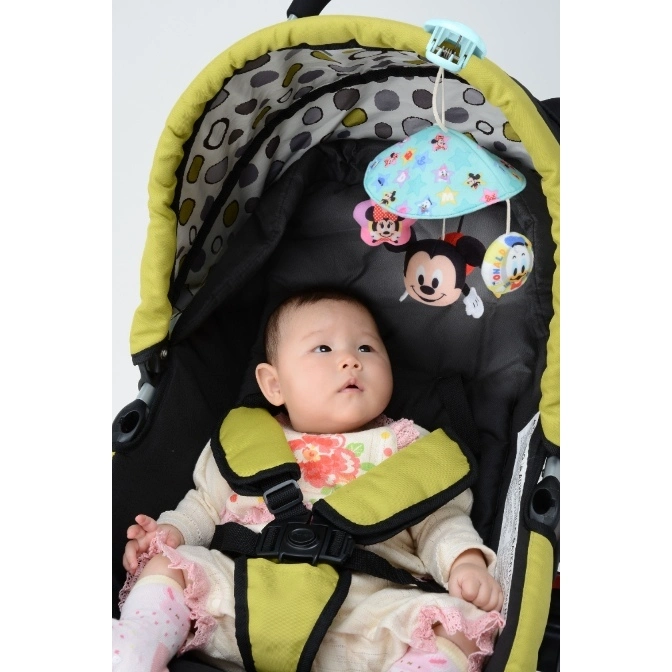  Baby in stroller with Disney character mobile toy hanging above. Safety harness is fastened.
