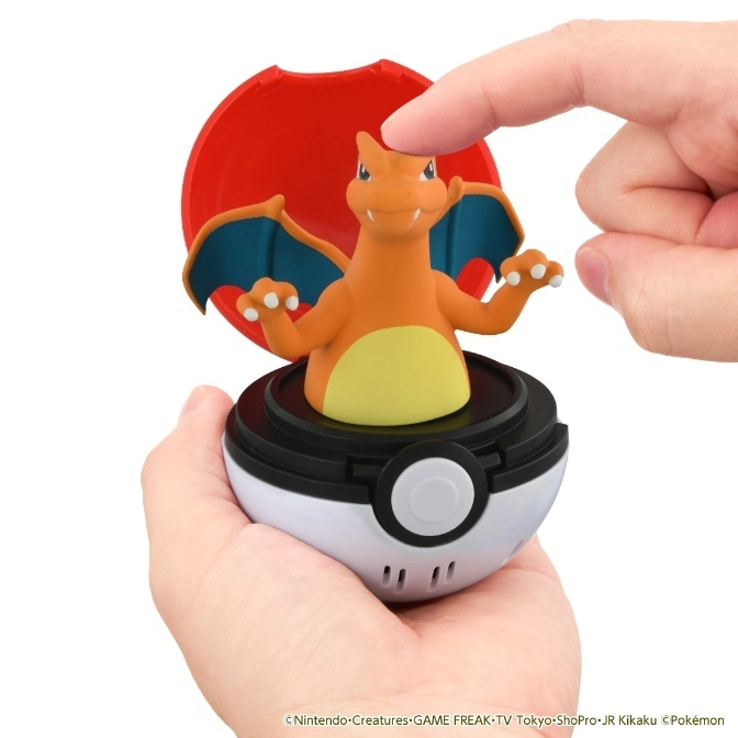  Charizard toy popping out of a Poké Ball held in someone's hands, with a finger about to touch it.