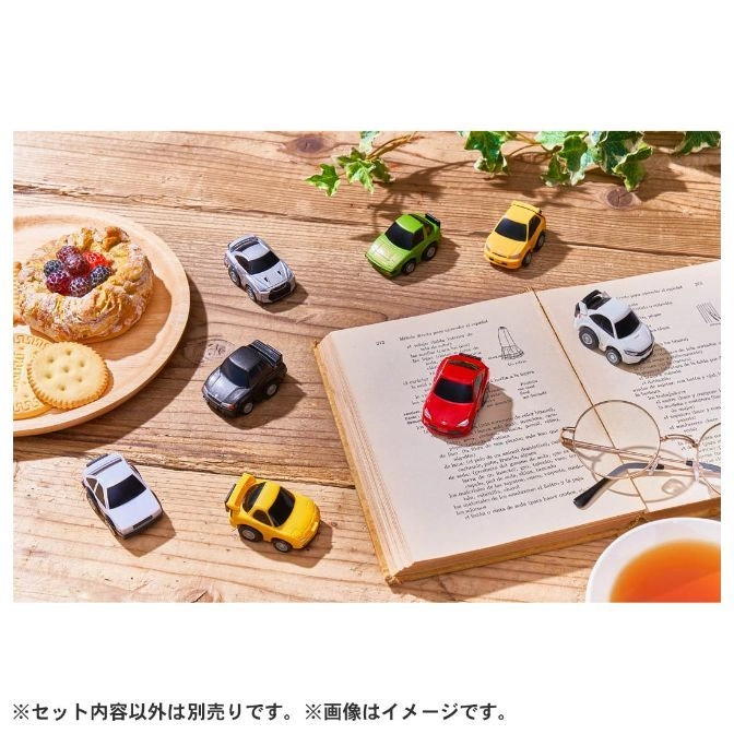  Colorful toy cars on a book near pastries and tea, creating a playful, cozy scene.