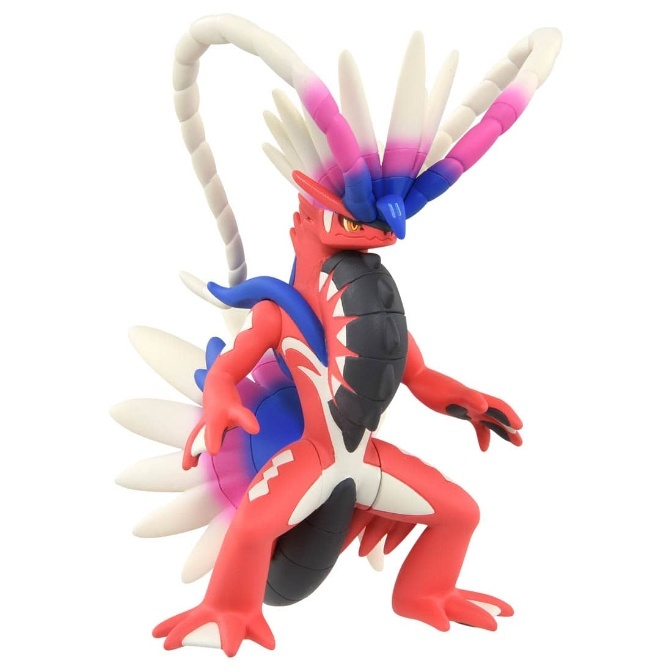Koraidon toy figure, red with white accents, blue and pink head feathers, standing pose.