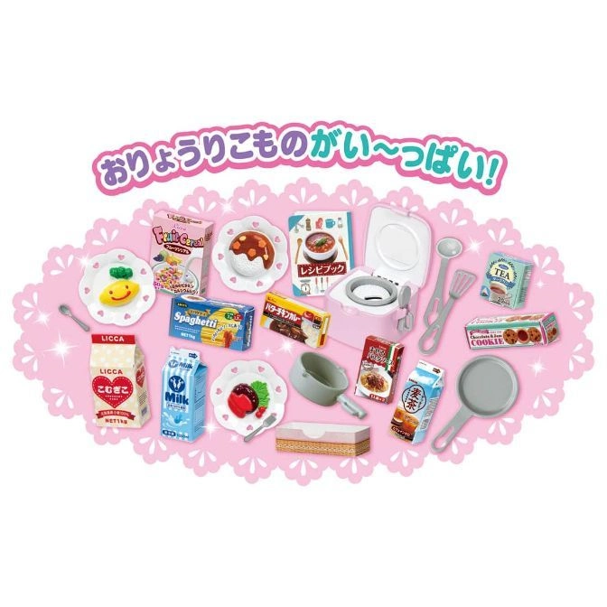 Toy kitchen set with miniature food boxes, plates, cookware, and a recipe book on a pink lace mat.