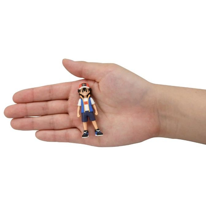  Ash Ketchum figurine in a hand, wearing a red cap, blue vest, and shorts.
