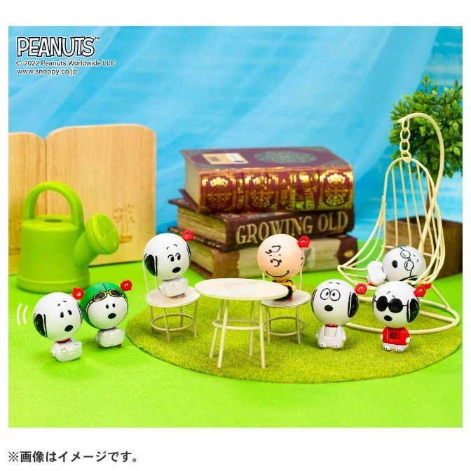  Peanuts figurines at a table, including Snoopy and Charlie Brown, with books and a swing in the background.