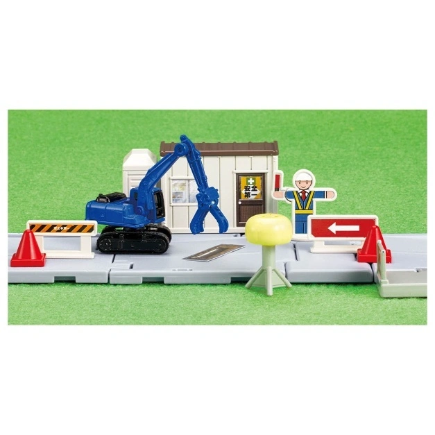  Toy construction site with a blue excavator, worker figure, building, and traffic cones.