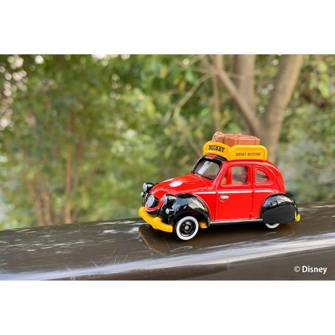  Red and black toy car with Mickey Mouse luggage on top, parked on a ledge.