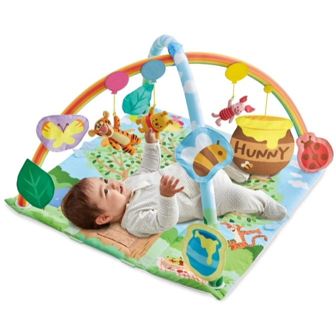 Baby on Winnie the Pooh play gym with hanging toys like Tigger, Piglet, and a honey pot.