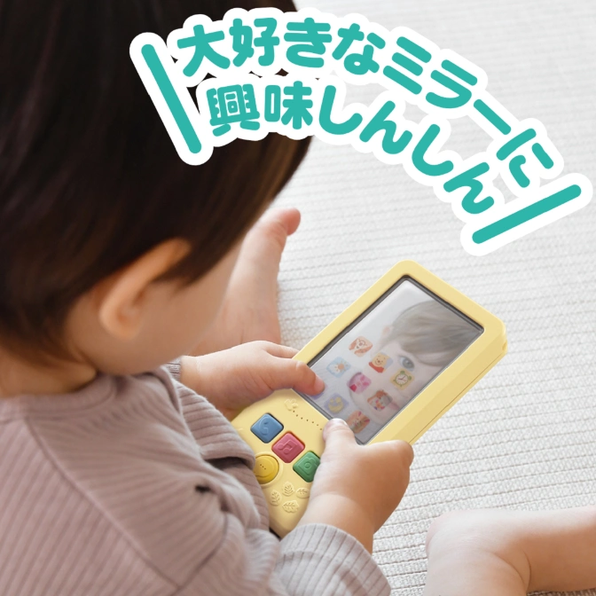  Baby playing with a yellow toy smartphone featuring a mirror screen and colorful buttons.