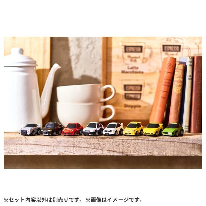  Toy cars lined up on a shelf with coffee cups and books in the background.