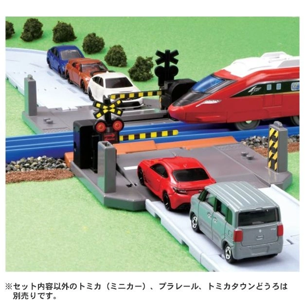 Toy train crossing with cars stopped at the barrier, including a red train and miniature vehicles.