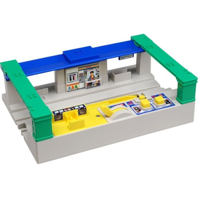 A toy train station with a blue roof, green supports, and a yellow platform.