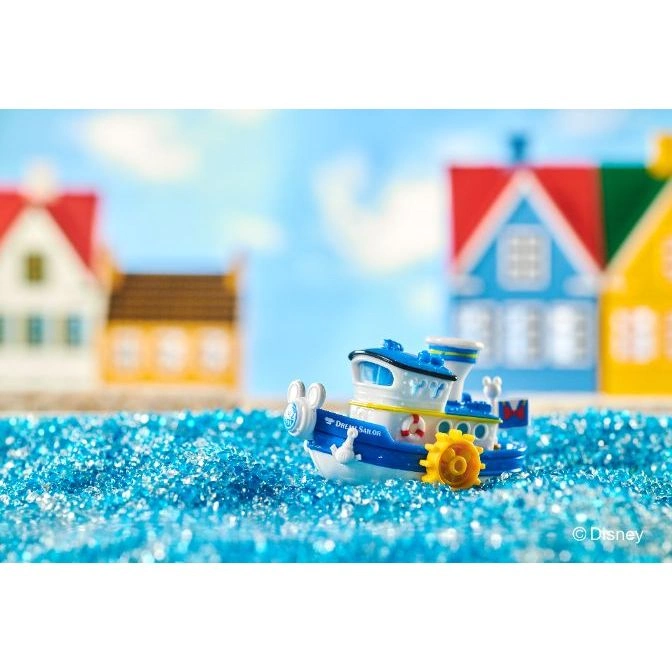  Toy boat "Dream Sailor" with Mickey Mouse details, on blue glitter "water" with toy houses in the background.