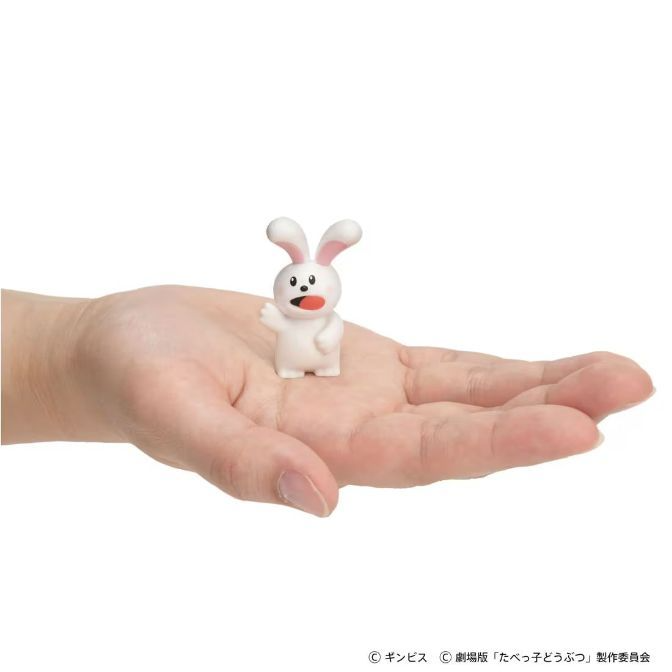  White rabbit toy figure standing on a hand, tongue sticking out.