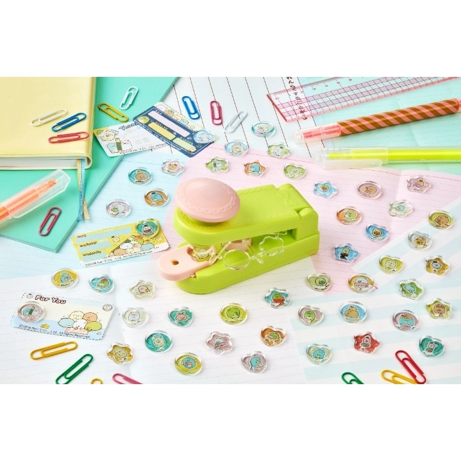  Green stapler with character-themed staples scattered around it on a patterned surface.