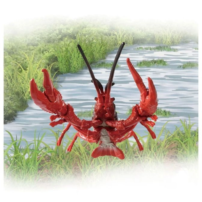  Red toy crawfish with large claws and antennae, set against a grassy, watery backdrop.