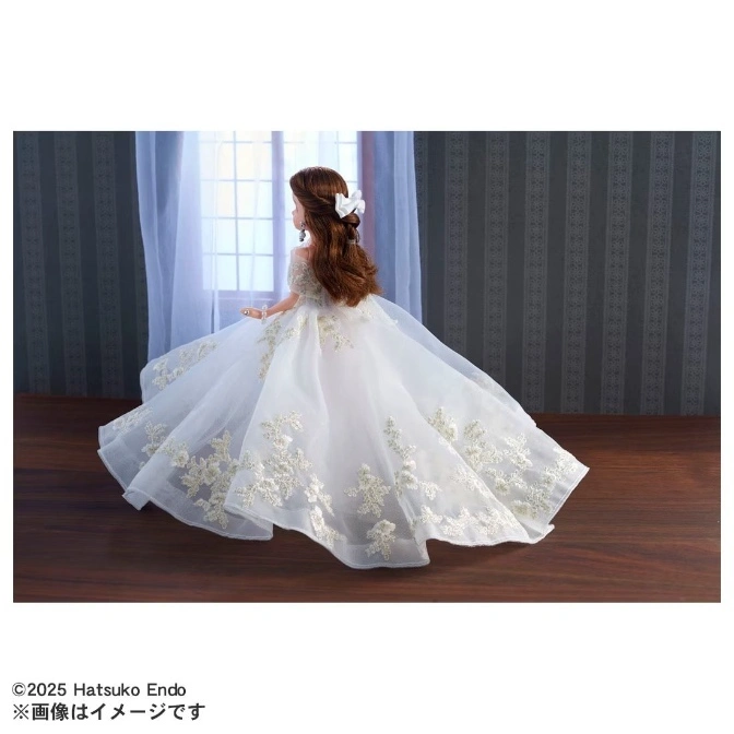  Doll in white lace wedding gown with train, hair bow, and earrings, facing away from viewer.