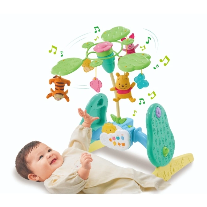 Baby lying under a Winnie the Pooh mobile with hanging plush toys and musical notes.