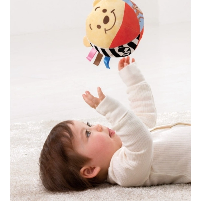  Baby reaching for a Winnie the Pooh sensory ball with colorful ribbons.