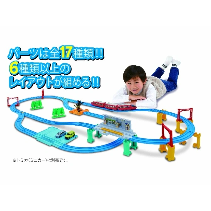  Toy train set with tracks, cars, and a child playing. Includes station, trees, and bridge.