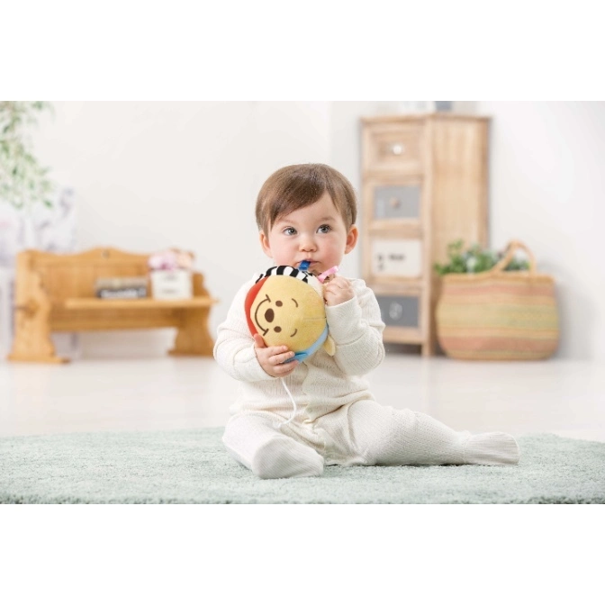  Baby chewing on a plush toy with a smiling face, red and blue accents, and a striped top.