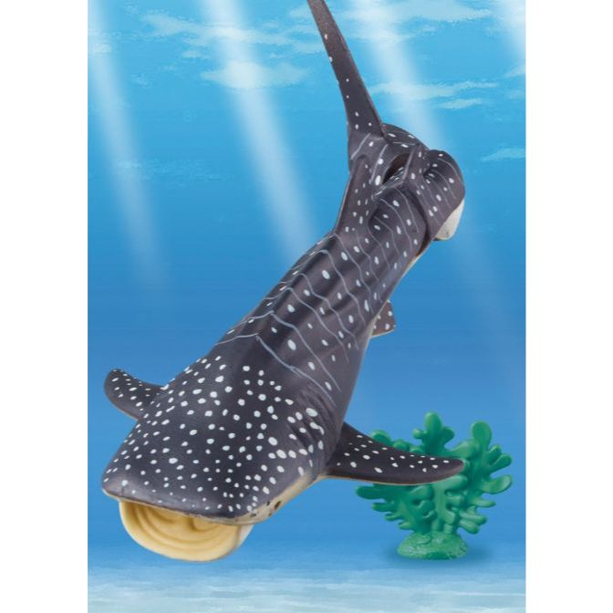  Toy whale shark with white spots swimming near green coral in a blue ocean setting.