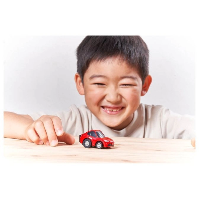  Smiling child plays with a small red toy car on a wooden surface.