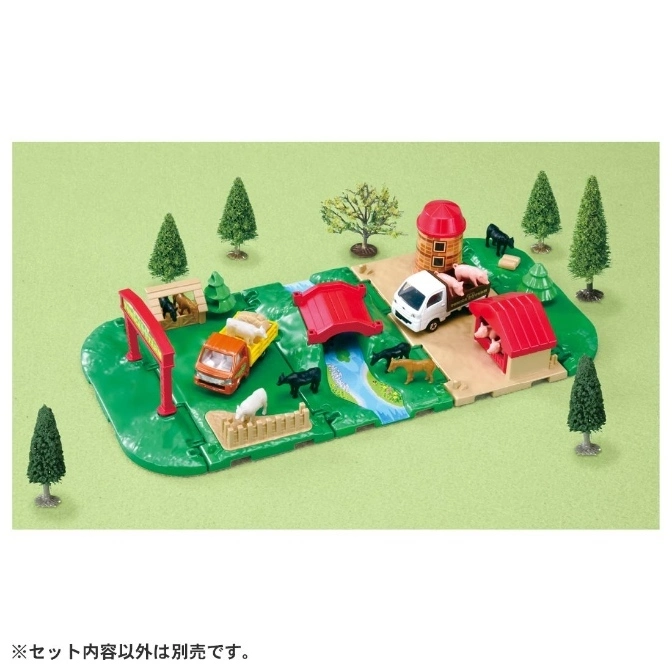 Toy farm set with trucks, animals, barn, bridge, and trees on a green playmat.