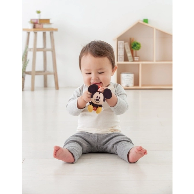  Baby sitting, holding a Mickey Mouse plush toy.