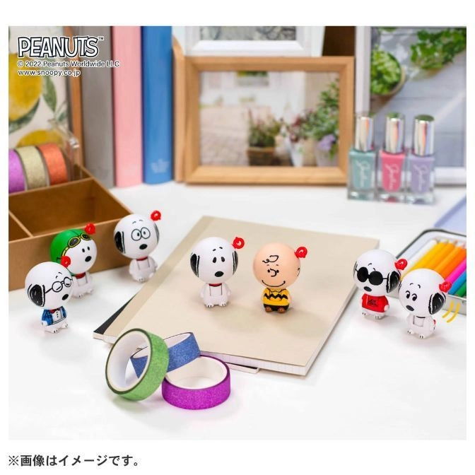  Snoopy and Charlie Brown toys with red antennae on a notebook with colorful tape rolls.