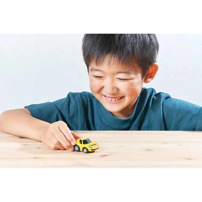  Smiling boy playing with a yellow toy car on a wooden table.