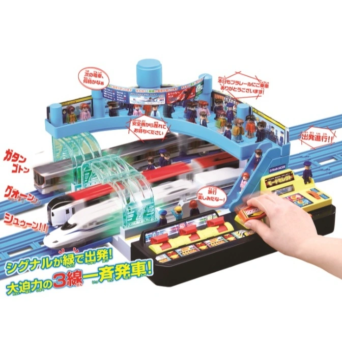  Toy train station with 3 tracks, control panel, and miniature figures. A hand presses a button.