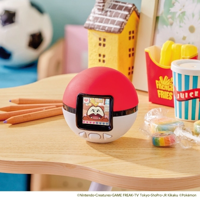  Pokémon Poké Ball virtual pet toy with a cartoon character on screen, surrounded by toy food and pencils.