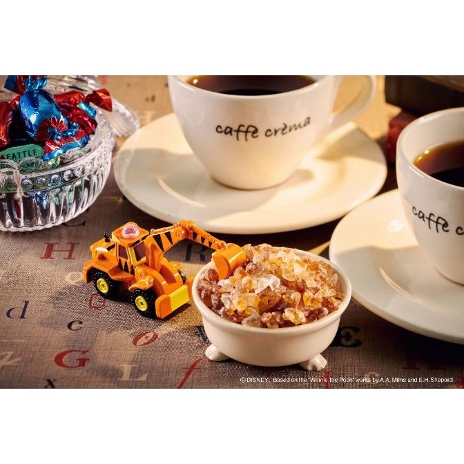  Toy excavator digging into a bowl of sugar crystals, next to coffee cups and candy.