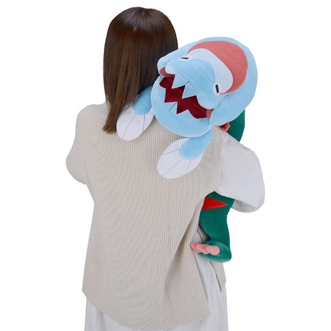  Woman holding a blue Gible plush toy with red accents and white fins over her shoulder.