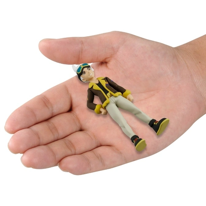  Small toy figure of a boy with goggles, brown jacket, and khaki pants lying in a hand.