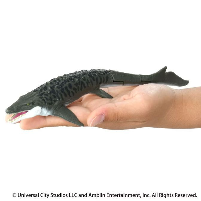  Mosasaurus toy figure in hand, dark gray with black spots, articulated tail.