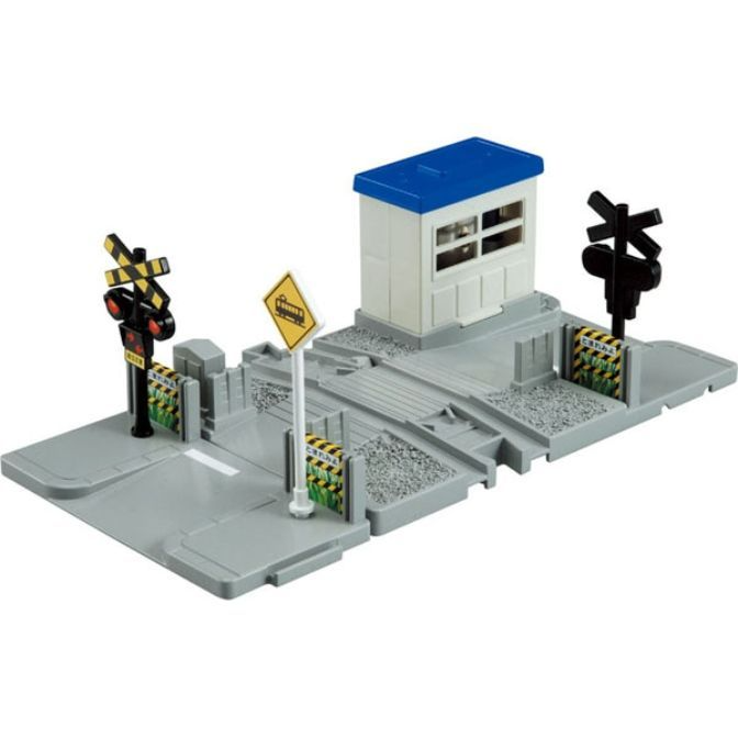 A toy train crossing with a small building, signs, and barriers.