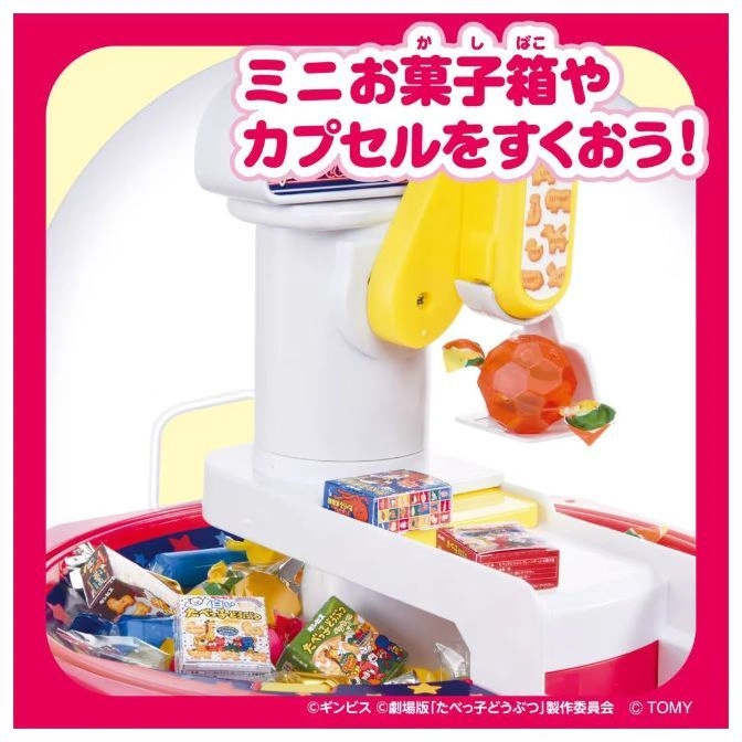  Toy candy dispenser with animal crackers and capsules. Yellow arm scoops an orange ball.