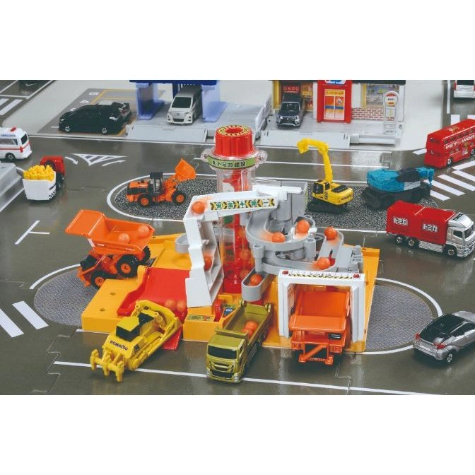 Toy construction site with trucks, crane, and ball run, set on a playmat with roads and buildings.