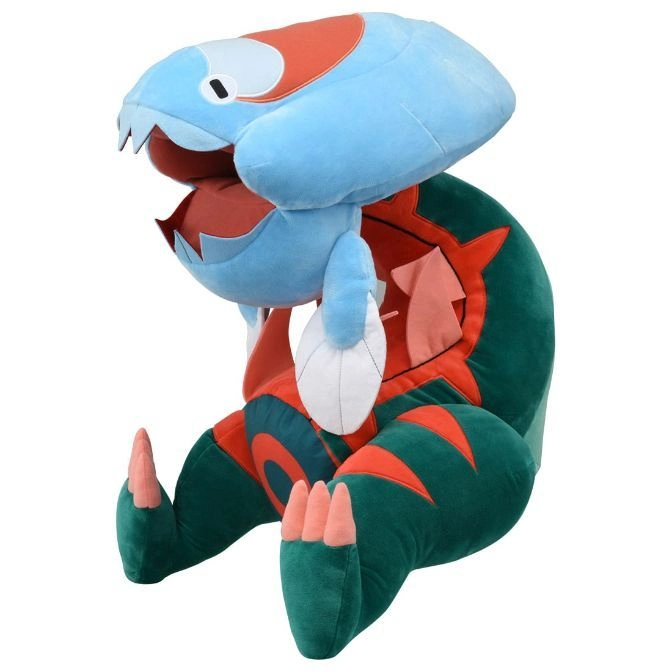Plush Drakloak toy with blue head, green body, and orange accents, sitting upright.